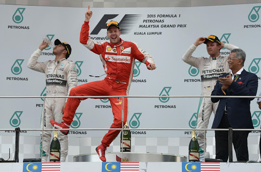 TOPSHOTS Ferrari's German driver Sebastian Vettel (C) celebrates on the podium in front of second placed Mercedes AMG Petronas F1 Team's British driver Lewis Hamilton (L) and Mercedes AMG Petronas F1 Team's German driver Nico Rosberg (R) during the Formula One Malaysian Grand Prix in Sepang on March 29, 2015. AFP PHOTO / MOHD RASFAN