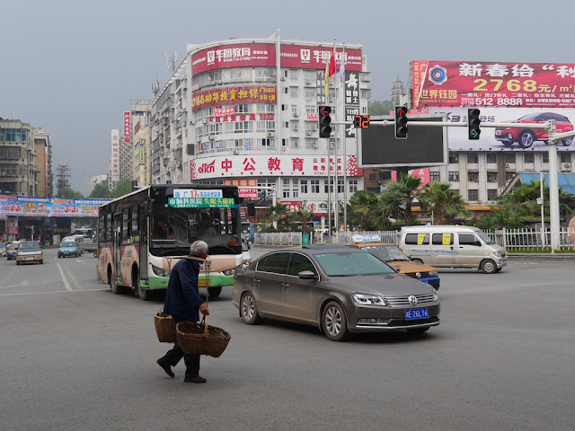 man carrying two baskets on a pole across the intersection of Wuyi Road and Dongfeng Road