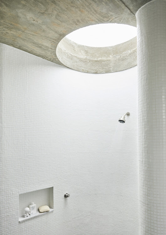 The curvaceous shower in the main bathroom is illuminated from above by a circular skylight and clad in white mosaic tiles from Douglas Jones.