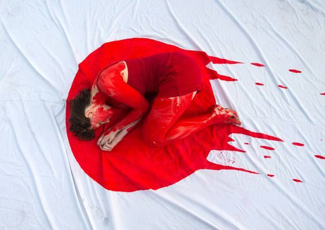 An anti-whaling protester, covered in mock blood, curls up in a representation of the Japan flag. Photo: Captain Paul Watson