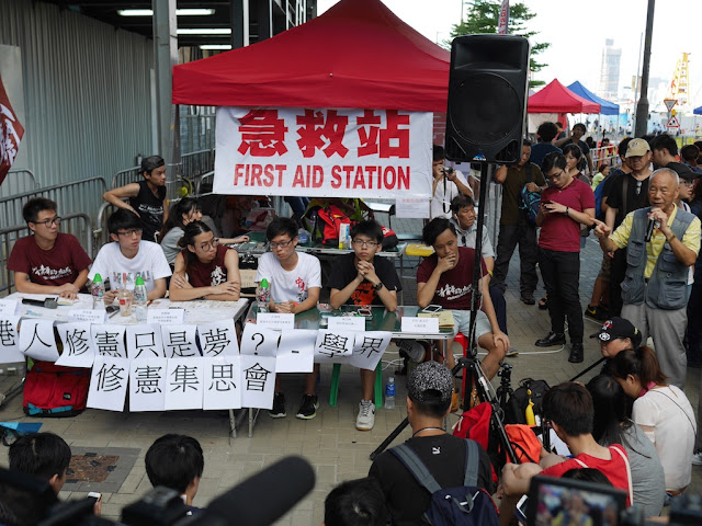 man giving a speech with Joshua Wong in attendance