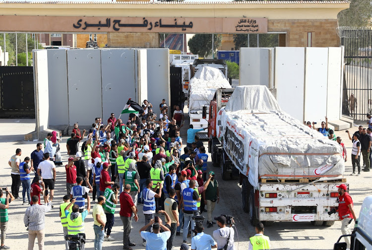 Egyptian volunteers gather and celebrate with a Palestinian flag next to trucks carrying humanitarian aid from Egyptian NGOs driving through the Rafah crossing from the Egyptian side, amid the ongoing conflict between Israel and the Palestinian Islamist group Hamas.