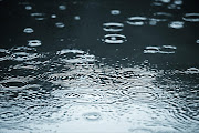Close-up of a puddle with rain drop ripples - Stock image