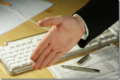 Photo of the arm and hand of someone ready to shake hands in front of a computer keyboard