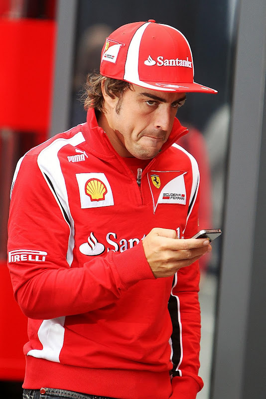 Фернандо Алонсо идет по паддоку Хунгароринга с телефоном в руках на Гран-при Венгрии 2011