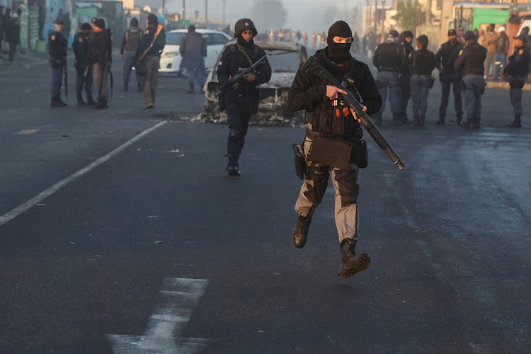 Security officials run past a burnt-out vehicle in Nyanga during the ongoing strike by taxi operators in Cape Town, August 7 2023. Picture: ESA ALEXANDER/REUTERS