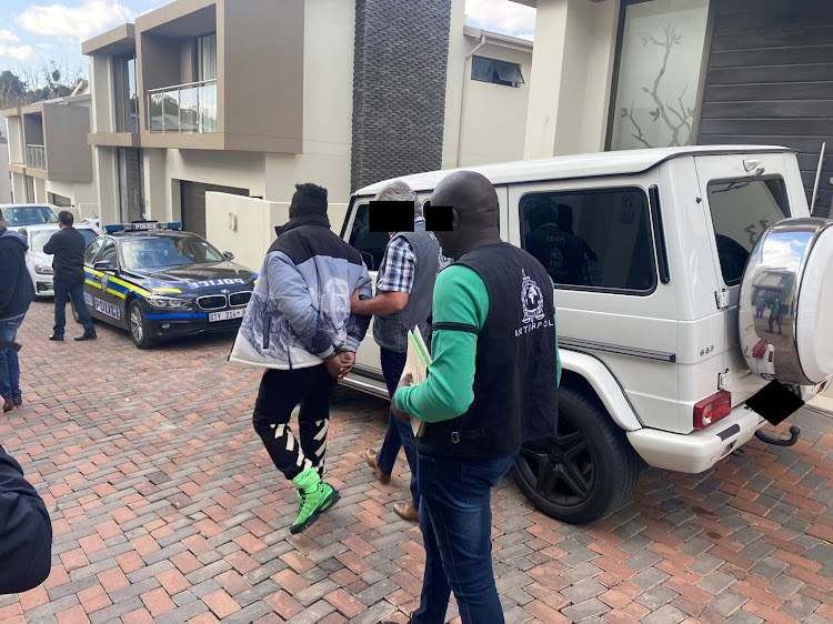 The alleged cybercrime kingpin walks past his Mercedes-Benz G63 luxury SUV as he is taken into custody by Interpol officers.