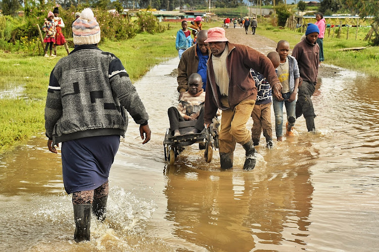 Residents of Kageraini village in Kinangop constituency assist a disabled child cross a flooded section of the road