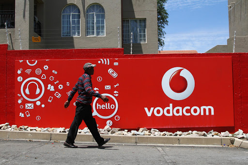 A pedestrian walks past a Vodacom-branded billboard at a taxi rank near Vodaworld, the headquarters of Vodacom Group Ltd. File photo