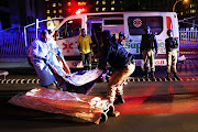 Selby Cindi, from Johannesburg Forensic Pathology Services, and a Johannesburg metro police officer lift the body of an accident victim from a street in the Johannesburg CBD.