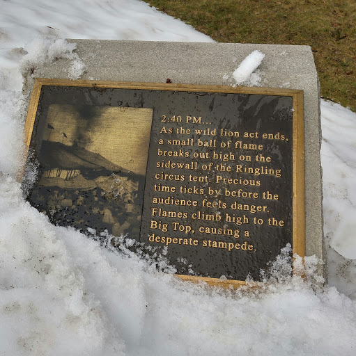 The first in a series of plaques about the Hartford Circus Fire. It reads: "2:40 PM...As the wild lion act ends, a small ball of flame breaks out high on the sidewall of the Ringling circus tent....