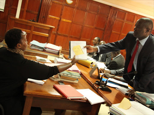 THEY STILL OWE ME: Lawyer Tom Ojienda (R) hands documents to a clerk at the Milimani law courts yesterday. Photo/PHILIP KAMAKYA
