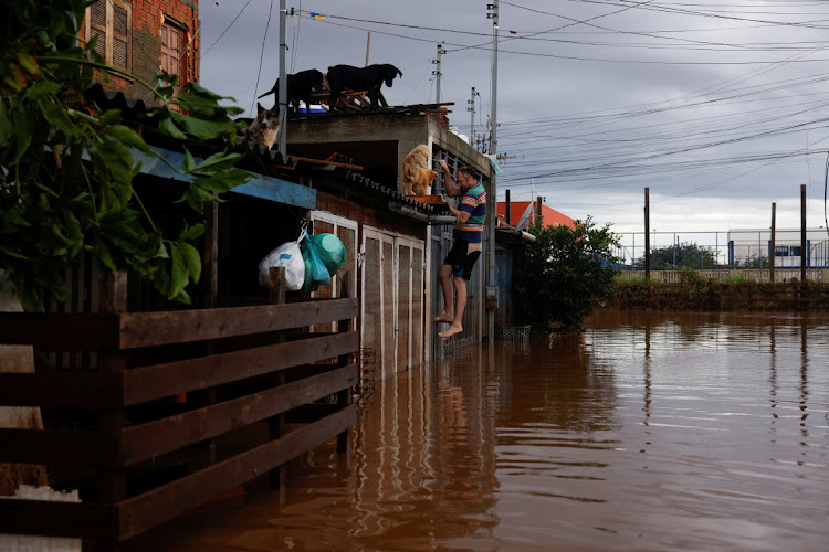 A man climbs a gate to access a house in a flooded area in Eldorado do Sul, Rio Grande do Sul state, Brazil May 8, 2024.