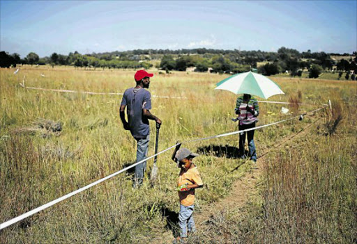 LAND ISSUE: A couple and their child are seen on vacant land marked with tape in Olievenhoutbosch near Centurion Picture: Reuters