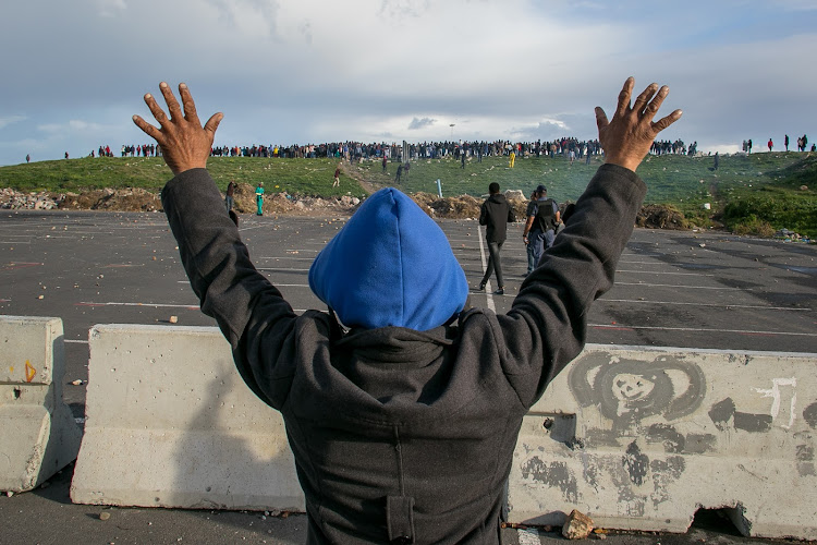 A Hermanus resident holds up his hands in an attempt to stop protesters from throwing rocks at police on July 13, 2018.
