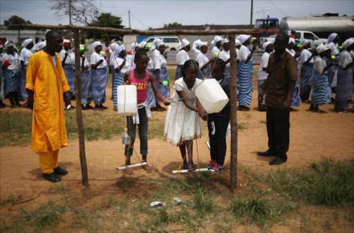 Girls wash their hands in disinfectant water as women pray for an end of the Ebola epidemic.