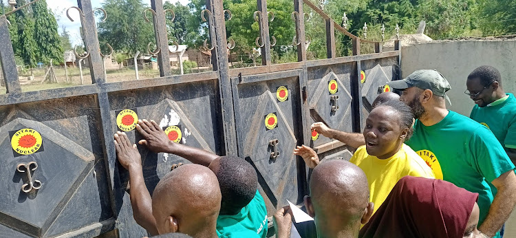 Environmental activists stick anti-nuclear stickers on the gate of the Chumani social hall in Chumani, Kilifi county, on Wednesday.