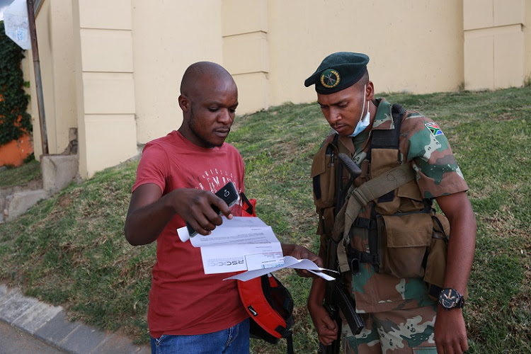 A SANDF officer checks the permits of an essential worker