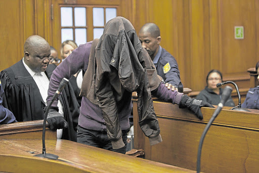One of the accused in the Anni Dewani murder case, Xolile Mngeni, hides his face as he finds his way into the dock at the Cape Town High Court. File photo.