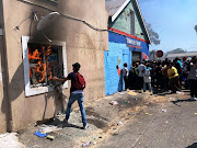 A building near Goodwood magistrate's court burns as a crowd gathers outside a shop that was later looted on February 21 2020.