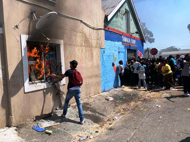 A building near Goodwood magistrate's court burns as a crowd gathers outside a shop that was later looted on February 21 2020.