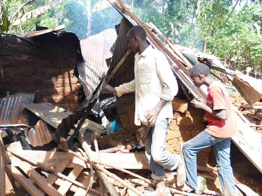 in a white shirt Dennis Mwangi with his cousin Anthony Murimi try to salvage their uncles property after it was torched by members of the public after he attacked his mother with a panga in Kirinyaga county