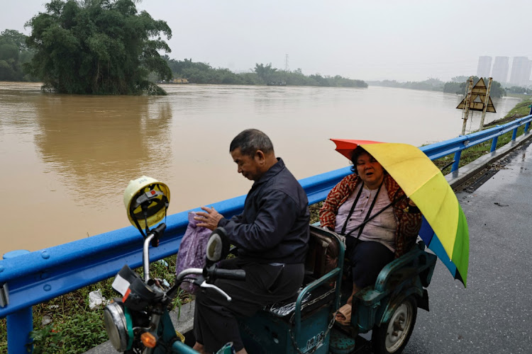 Residents ride on a scooter near a flooded river, following heavy rainfall in Qingyuan, Guangdong province, China, on April 22 2024.