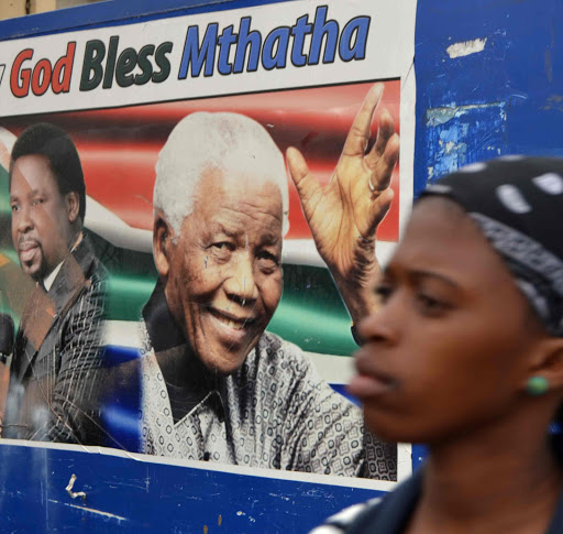 LONG TIME COMING: A young girl walks past a poster with the faces of Nigerian celebrity televangelist T B Joshua and late former president Nelson Mandela in Sprigg Street, Mthatha. A team of South Africans are in Nigeria to bring back some of the bodies that are still in that country after Joshua’s church collapsed last year Picture: LOYISO MPALANTSHANE