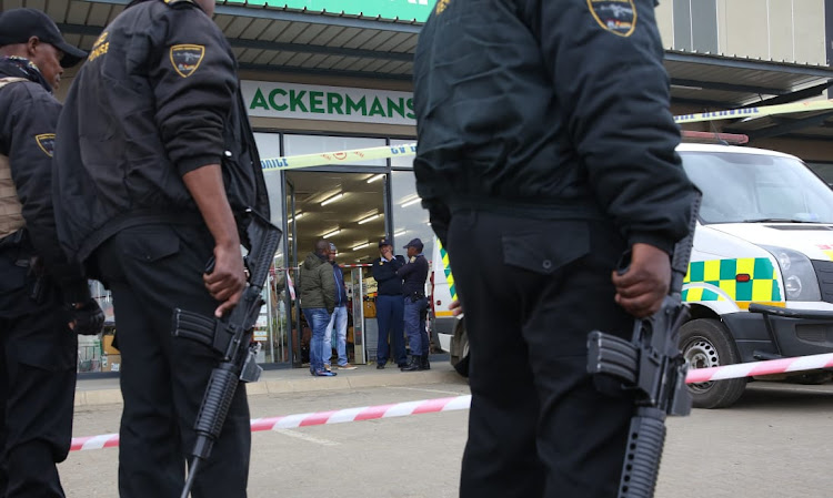 Members of security company ACSU watch police start their investigation at the Ackermans branch in Wesselton township, outside Ermelo.