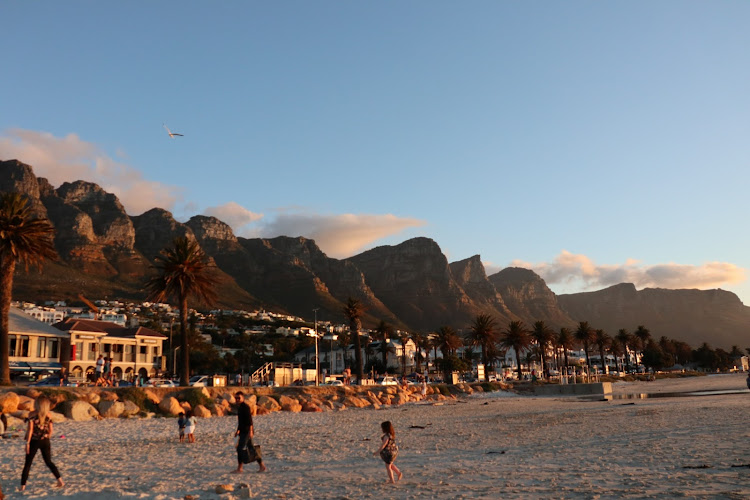 Families vacate the beach as party-goers start to populate the stretch of bars and restaurants opposite the beach in Camp's Bay at the foot of the Twelve Apostles mountain range.