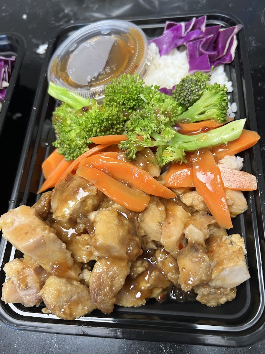 A To Go container of General Tso. Chicken thighs, and veggies with white rice in a lightly spicy  and finger licking sauce.