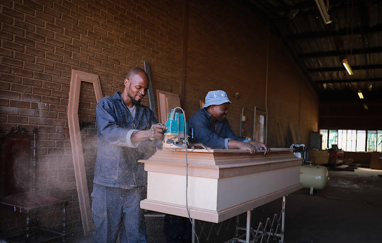 Sam Masango and Mandla Mazibuko, carpenters at Malusi Coffin Manufacturers in Emdeni, Soweto trip of the edges on an already assembled coffin. The manufacturers say demand for coffins and caskets has gone up due to the number of Covid-19 related deaths.