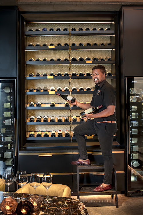 Sommelier Reggie Phege in front of a curated wine cellar devoted entirely to celebrating SA fine wine.