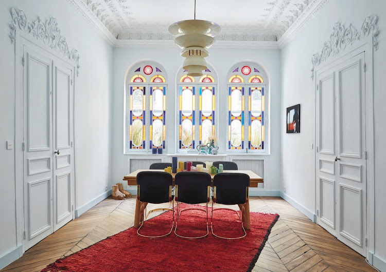 The spectacular stained-glass windows infuse the dining room with an almost spiritual atmosphere. Perfectly preserved, these windows are original features dating to the 18th century. The light is a mid-century Danish design from a flea market, the bright-red Moroccan rug from Bleu de Fès. The vintage 1970s leather-andbrass dining-room chairs are from Brussels, and the white server is a fixture in the apart - ment from a previous owner.