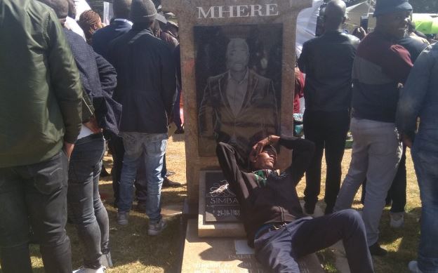 A man rests on the tombstone of late TV personality Simba Mhere.