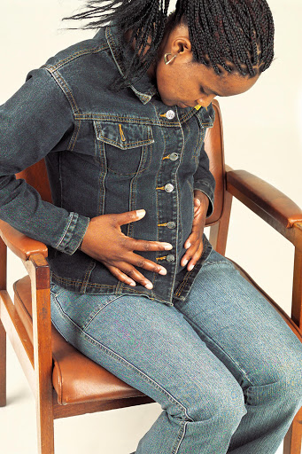 A pregnant woman sitting in a chair examining her tummy.