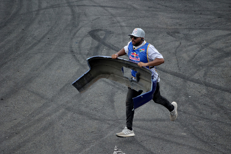A man runs with a car bumper that fell off a car's competitor.