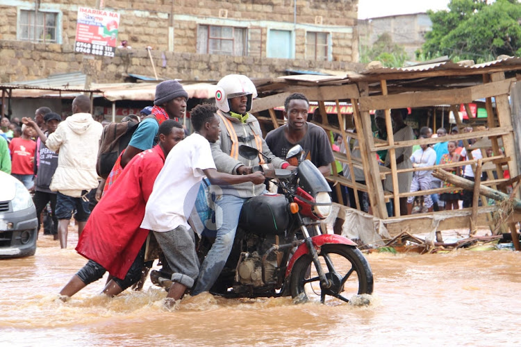 Locals help a motorist to cross a flooded road at a bridge connecting Mwiki and Kasarani on April 24, 2024.