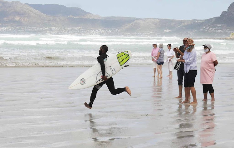 A surfer is applauded as he races into the waves in Muizenberg on January 30 2021 during a protest against the lockdown beach ban.