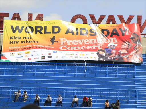 People sit near a banner during world AIDS day at Nyayo stadium. Photo/Monicah Mwangi