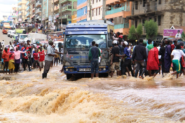Residents help a matatu that almost lost control to cross a flooded road at a bridge connecting Mwiki and Kasarani on April 24, 2024.