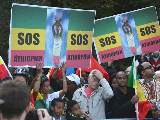 Marathon runner Feyisa Lilesa (L) of Ethiopia and supporters hold placards as they stage a protest against Ethiopian government near the finish line at the Berlin marathon in Berlin, Germany, September 25, 2016. /REUTERS