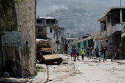 People walk past a damaged car in the Carrefour Feuilles neighborhood, which was deserted due to gang violence, in Port-au-Prince, Haiti March 19, 2024. 