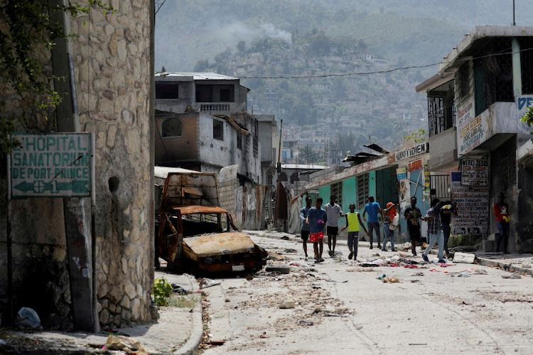 People walk past a damaged car in the Carrefour Feuilles neighborhood, which was deserted due to gang violence, in Port-au-Prince, Haiti March 19, 2024.