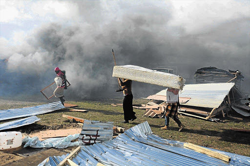 Women carry away their belongings, left, before workers dismantle their homes in Lwandle. File photo.