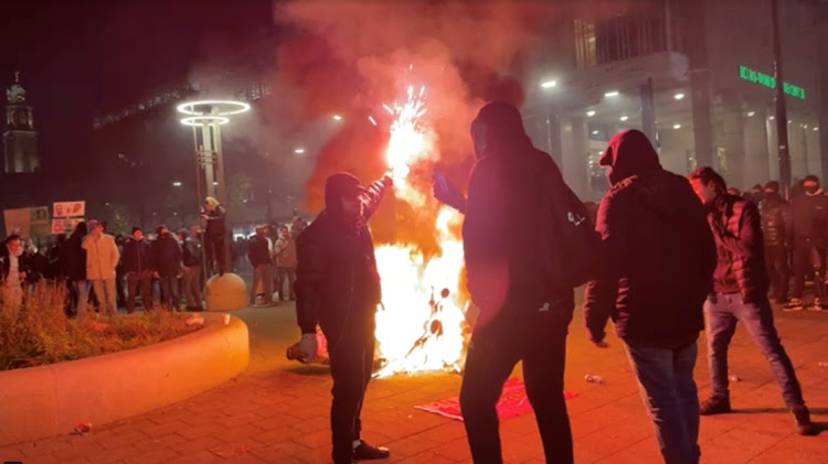 A man stands with a flare as protesters watch a motorcycle burning in Rotterdam, the Netherlands, November 20, 2021, in this screen grab obtained from a social media video.