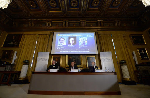 (L-R) Sven Lidin, Staffan Normark and Gunnar Karlstrom sit in front of a screen displaying the portraits of scientists (L-R) Martin Karplus, Michael Levitt and Arieh Warshel during a press conference to announce the laureates of the 2013 Nobel Prize in Chemistry on October 9, 2013 at the Nobel Assembly at the Royal Swedish Academy of Sciences in Stockholm. US-Austrian Martin Karplus, US-British Michael Levitt and US-Israeli Arieh Warshel won Nobel Chemistry Prize for the development of multiscale models for complex chemical systems.