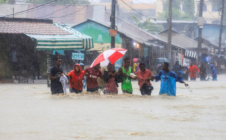 People wade through flood waters along a street following heavy rains in Kisauni district of Mombasa, Kenya, on November 17 2023.