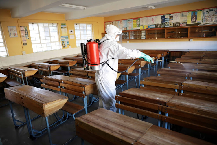 A worker wearing protective gear sprays disinfectant in a classroom at Groenvlei High School in Lansdowne, Cape Town.