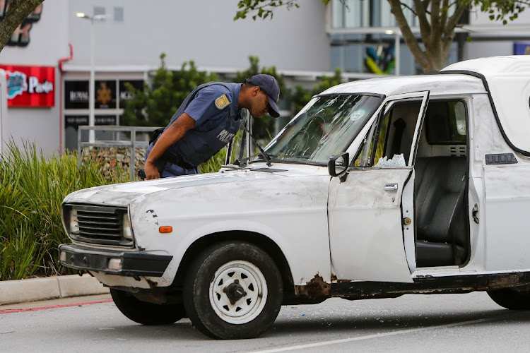A police officer inspects the bakkie in which a suspected robber was shot in the neck at Baywest Mall early on Monday
